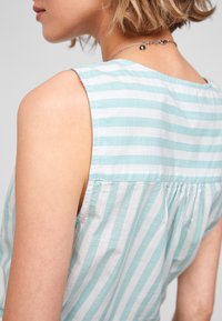 Top senza maniche a righe in azzurro chiaro e bianco, con una texture morbida e dettaglio arricciato sul retro, dotato di un semplice scollo rotondo.