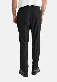 Melnas piegrieztas bikses ar gludu tekstūru, kas aprīkotas ar divām aizmugurējām kabatām un taisna kāju dizainu, apvienotas ar melnām kurpēm.