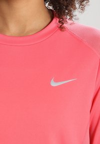 Nike träningsskjorta i klar rosa, med rund necklinje, texturerade axelpaneler och en liten silverlogga på bröstet.