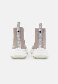 Zapatillas altas de punto en color beige con suelas de goma blanca. Presenta tiradores verticales con texto y un detalle de logo en la parte trasera.