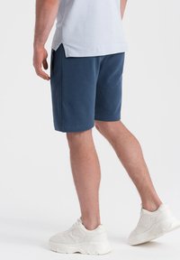 Shorts de sport bleu marine avec une coupe décontractée, poches latérales et texture douce. Associés à des baskets blanches imposantes.