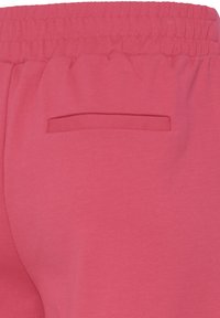 Gros plan sur un pantalon à taille élastique rose avec une poche passepoilée à l'arrière, dotée d'un bord en tissu au-dessus de l'ouverture de la poche.