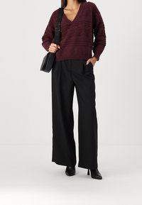 Vinröd stickad tröja med V-ringning och texturerade mönster, kombinerad med svart högmidjad byxa med vida ben och svarta stövlar med klack.