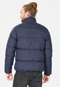 Doudoune marine avec un motif matelassé vertical, col montant et poignets élastiques. Texture douce et lisse avec une surface légèrement brillante.