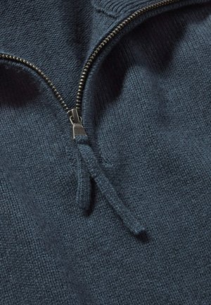 Dunkelblauer gestrickter Pullover mit hohem Kragen, ausgestattet mit einem silbernen Metallreißverschluss und einem strukturierten Stoff, der eine Nahaufnahme des Materials zeigt.