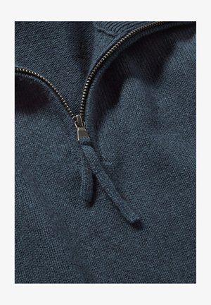 Dunkelblauer gestrickter Pullover mit hohem Kragen, ausgestattet mit einem silbernen Metallreißverschluss und einem strukturierten Stoff, der eine Nahaufnahme des Materials zeigt.