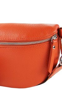 Sac bandoulière rond en cuir orange avec une surface texturée, une fermeture éclair argentée et une sangle réglable. Présente un design minimaliste.