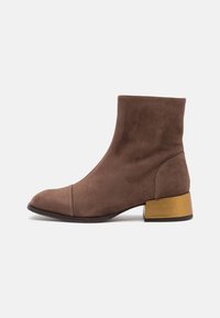 Brązowy zamszowy botek za kostkę z zaokrąglonym noskiem i krótkim, masywnym metallicznym złotym obcasem. Gładka tekstura z minimalnymi detalami szycia.