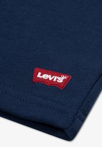 Tissu en coton bleu marine avec un tricot texturé ; présente un patch logo Levi's rouge cousu sur le pli, mettant en valeur l'identité de la marque.