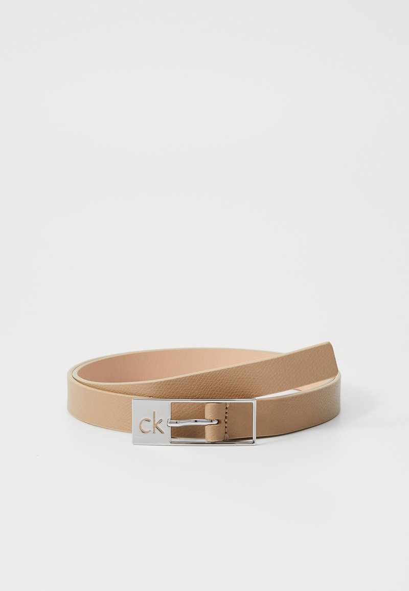 Lichtbeige leren riem met een gladde textuur. Heeft een zilveren metalen gesp met het reliëf "ck", wat een minimalistisch ontwerp tentoonstelt.