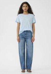 Ljusblå t-shirt med kort ärm och rund halsringning, ihop med vida, blekta blå jeans. Modellen bär svarta flip-flops. En enkel, avslappnad outfit.