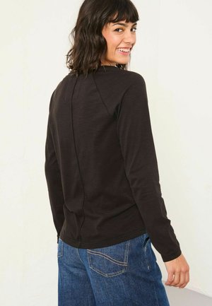 Schwarzes Langarmshirt mit rundem Halsausschnitt und einer Rückennaht-Detail. Kombiniert mit blauen Denim-Jeans. Glatte Textur und taillierte Passform.