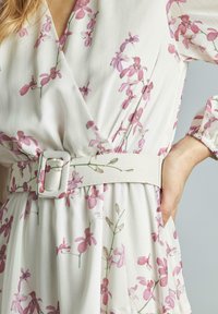 Abito a portafoglio floreale in tessuto leggero con motivo di orchidee rosa. Presenta una cintura ampia con fibbia quadrata, maniche lunghe elasticizzate e gonna plissettata.
