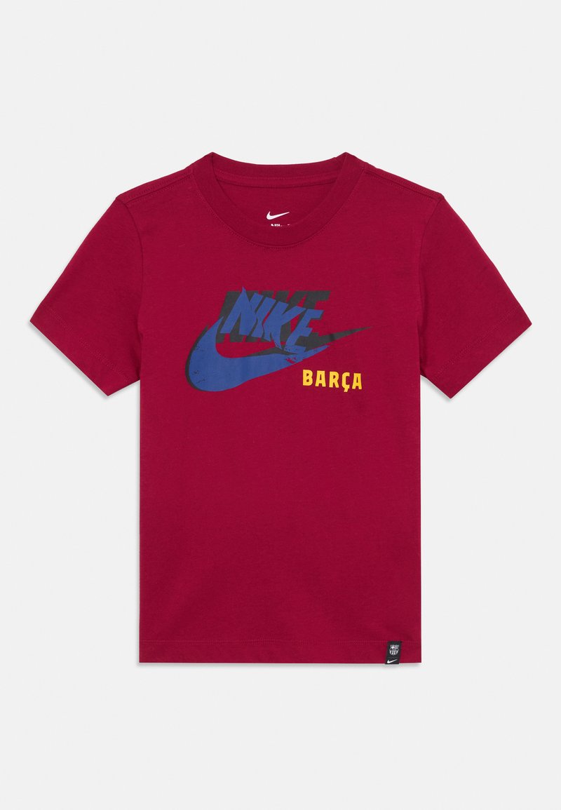 Rdeča bombažna majica s kratkimi rokavi, ki prikazuje grafiko v modri in črni barvi z napisi "NIKE" in "BARÇA" v rumeni. Ima krožni ovratnik.