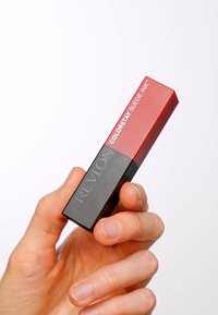 Produkt do ust Revlon Colorstay Suede Ink w matowym czerwonym kolorze, umieszczony w czarnym prostokątnym opakowaniu z wytłoczonym logo po boku.