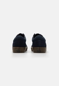 Marineblå semskede sneakers med teksturert overdel, brun gummisåle og trekkrem bak. Minimalistisk design med kontrastfarger.