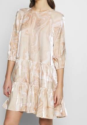 Vrouw draagt een glanzende beige-witte jurk met marmeren patroon, driekwart ballonmouwen en een gelaagde rok boven de knie.