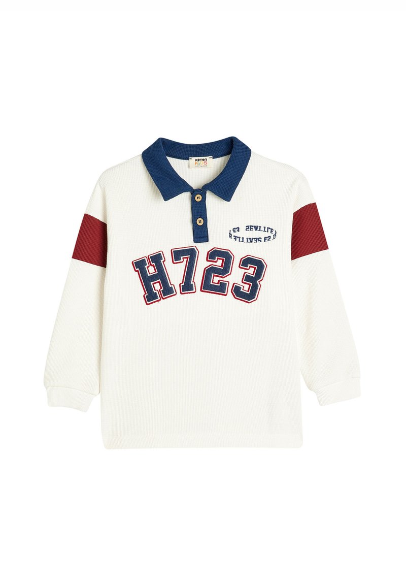 Camisa polo de manga larga blanca con cuello azul marino, detalles rojos en las mangas y "H723" impreso en letras grandes en la parte frontal. Cierre de dos botones.