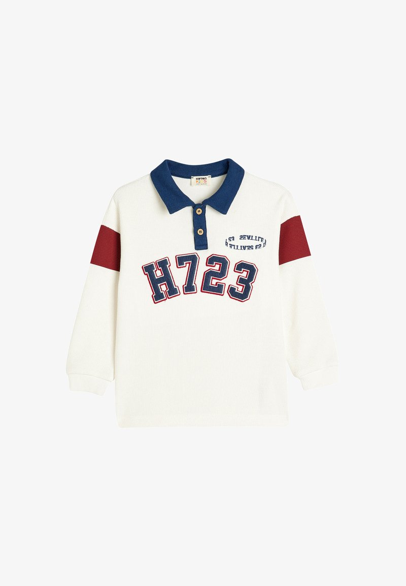 Camisa polo de manga larga blanca con cuello azul marino, detalles rojos en las mangas y "H723" impreso en letras grandes en la parte frontal. Cierre de dos botones.