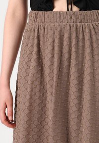 Jupe texturée marron avec un motif en diamants et des accents dorés, taille élastique et matériau léger et fluide.