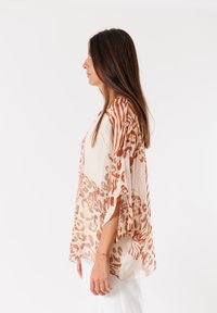 Blusa leggera, trasparente, di colore crema con stampa animalier marrone; vestibilità ampia, maniche larghe e design fluido.