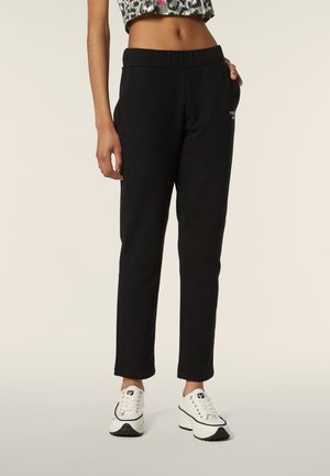 Pantaloni sportivi neri con vita elastica, vestibilità slim, tasche laterali e senza motivi visibili. Abbinati a sneakers bianche.