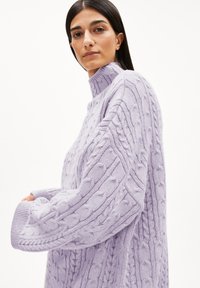 Übergroßer lavendelfarbener Strickpullover mit hohem Kragen, der eine Kabelstricktextur und grobe Muster am Körper und an den Ärmeln aufweist.