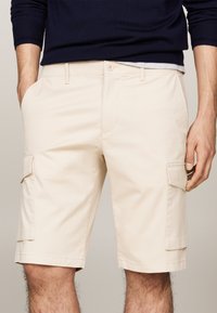 Shorts cargo beiges avec double poches latérales, une poche à rabat, fermeture à bouton et une texture lisse.