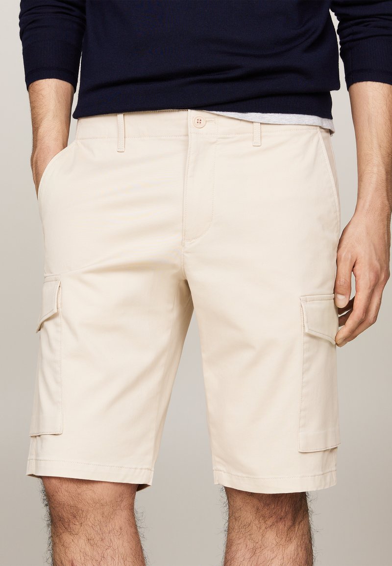 Shorts cargo beiges avec double poches latérales, une poche à rabat, fermeture à bouton et une texture lisse.
