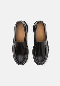 Scarpe slip-on in pelle nera con finitura liscia, punta arrotondata e suola in gomma testurizzata. L'interno presenta un dettaglio di branding impresso.