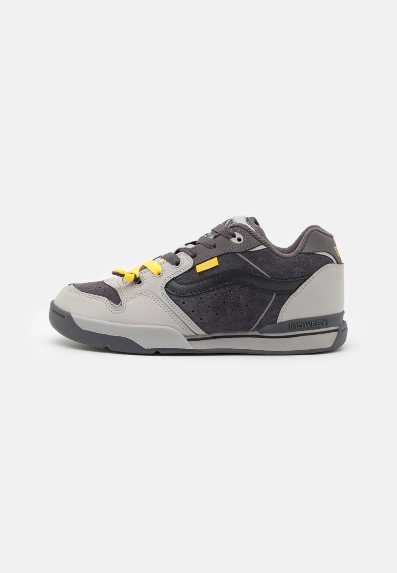 Chaussure de skate basse en gris et noir avec étiquette jaune sur les lacets et section contrastante de lacets jaunes, étiquette de marque visible sur la semelle et le côté.