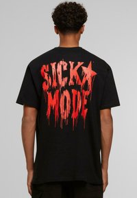 Must musta, millel on seljal suur punane voolav tekst "SICK MODE". Lühikesed varrukad ja tavaline lõige. Pehme puuvillane kangas.