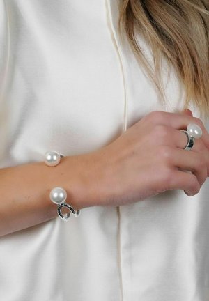 Silberarmband mit zwei großen weißen Perlen und einem gedrehten Design. Die Hand trägt auch einen passenden Silberring mit einem Perlenakzent.