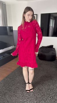 Röd spetsklänning med långa ärmar, hög hals och volangkant. Har ett blommönster och semi-transparent textur. Svarta remklackar.