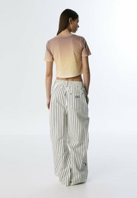 Háčkovaný crop top v gradientu od broskvové po béžovou s krátkými rukávy, spárovaný s bílými kalhotami s vysokým pasem a černými vertikálními pruhy.