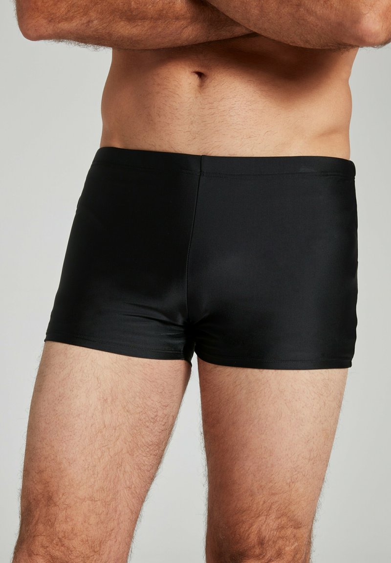 Schwarze Schwimmshorts aus einem glatten, dehnbaren Material. Sie haben ein eng anliegendes Design, ohne sichtbare Muster oder Hardwareakzente.