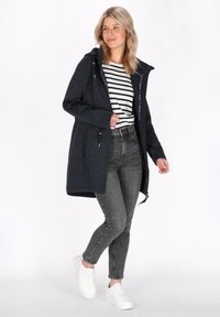 Tamsiai mėlynas tekstūruotas ilgas švarkas su kapišonu, raišteliu, užtrauktuku, derinamas su dryžuotu marškinėliais, pilkais džinsais ir baltais sportbačiais.