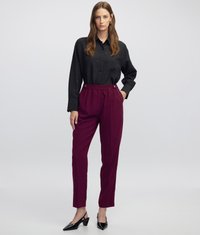 Camisa negra de botón con una textura sutil, combinada con pantalones burdeos ajustados y tacones negros puntiagudos, creando un look estilizado.