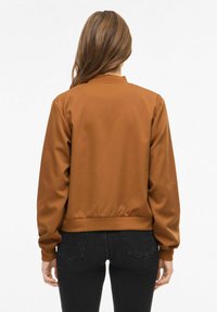 Jachetă bomber maro cu textură fină, manșete și tiv striate. Vedere din spate arată un design simplu, potrivit pentru uz casual.