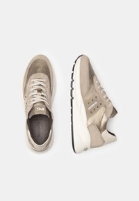 Beige Sneakers aus Wildleder und metallic Stoff, mit hellen Schnürsenkeln, Nietenakzenten und einer weißen Zwischensohle mit schwarzem Außenmaterial.
