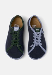 Deux paires de chaussures pour enfants exposées côte à côte ; l'une verte et marine avec des lacets, l'autre bleue et marine avec des lacets plus clairs.