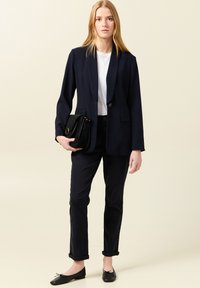 Marinblå blazer, vit t-shirt, mörka uppvikta jeans, svarta ballerinas. Svart handväska med strukturerat mönster och guldfinish. Enkel, skräddarsydd design.