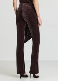 Pantaloni a zampa in velluto marrone con vita alta, spacco laterale e texture morbida. Abbinati a sandali neri con tacco alto.