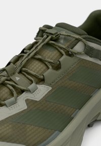 Grønn treningssko med teksturert stoff, ton-i-ton lisser, gummisåle og tre distinkte striper på siden med matt finish.