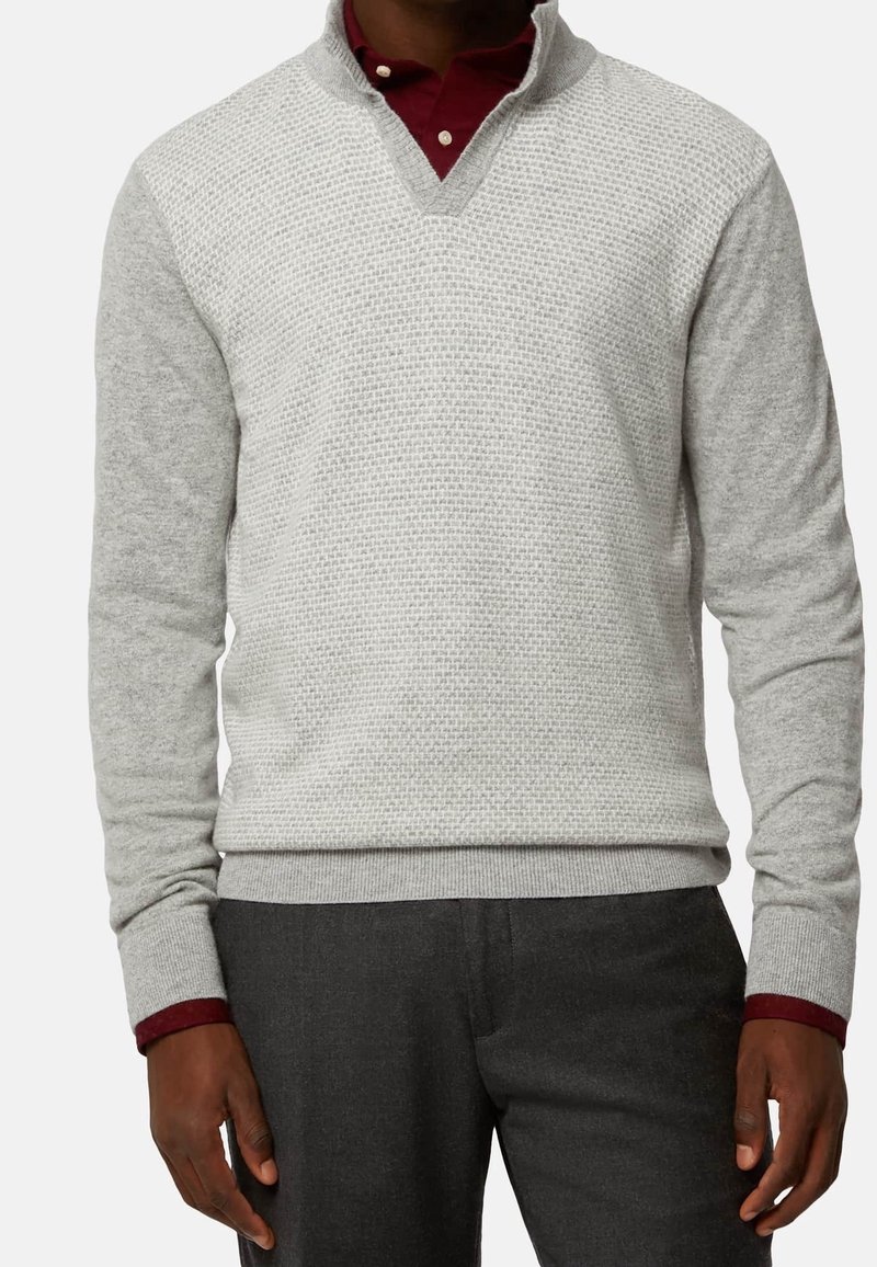 Maglione grigio testurizzato con scollo a V, maniche lunghe e polsini a coste. Indossato sopra una camicia con colletto bordeaux.