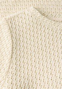 Vaalean beige neulepusero, jossa on teksturoitu avoin kudontamalli, pyöreä pääntie ja pehmeä kangas. Korostettu ribbineuloksella.