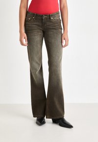 Dark green flared jeans with subtle fading, featuring orange stitching and classic pocket design. Paired with black pointed-toe boots.