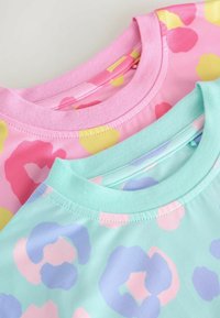 Dos camisetas con escote redondo: una en rosa con manchas amarillas y rosas, y la otra en menta con manchas lavanda y rosas. Tela suave.