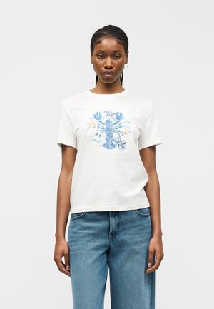 Woman with braided hair wearing white T-shirt featuring a blue lobster and marine design, paired with blue jeans, standing against a plain background.