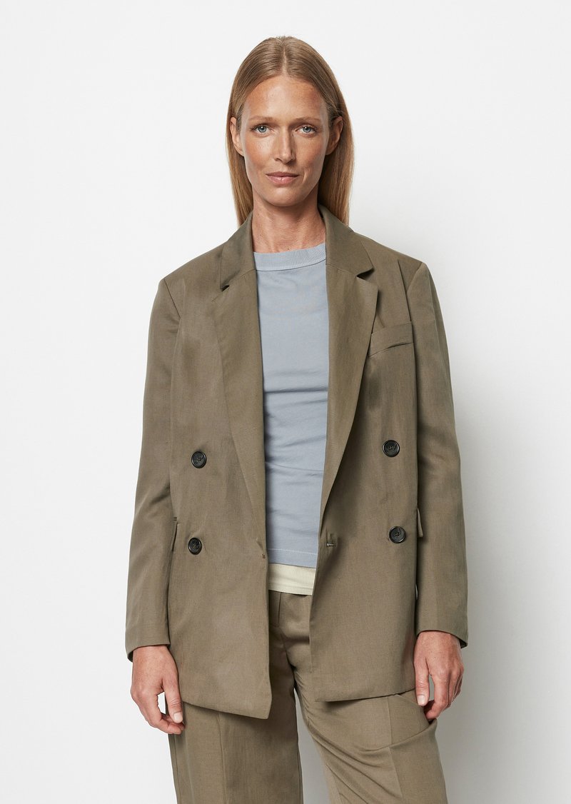 Dvojitě zapínaný olivově zelený lněný blazer se dvěma černými knoflíky. Stylizovaný přes světle šedý top s kulatým výstřihem. Hladká textura, strukturovaný design.